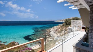 A coastal view from a balcony with clear blue sea, rocky terrain, and a stone wall. - Villa Santa Esmeralda Mykonos (Mykonos)