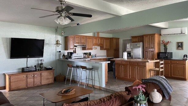 A spacious living room with a large sofa, a coffee table, and a TV. The kitchen area includes wooden cabinets, a refrigerator, and a microwave. - Relaxing Coastal Treasure on the canal (Corpus Christi)