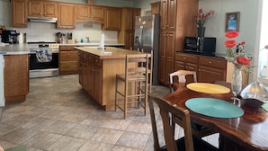 A modern kitchen with wooden cabinets, a central island, stainless steel appliances, and a dining area with a wooden table and chairs. - Relaxing Coastal Treasure on the canal (Corpus Christi)