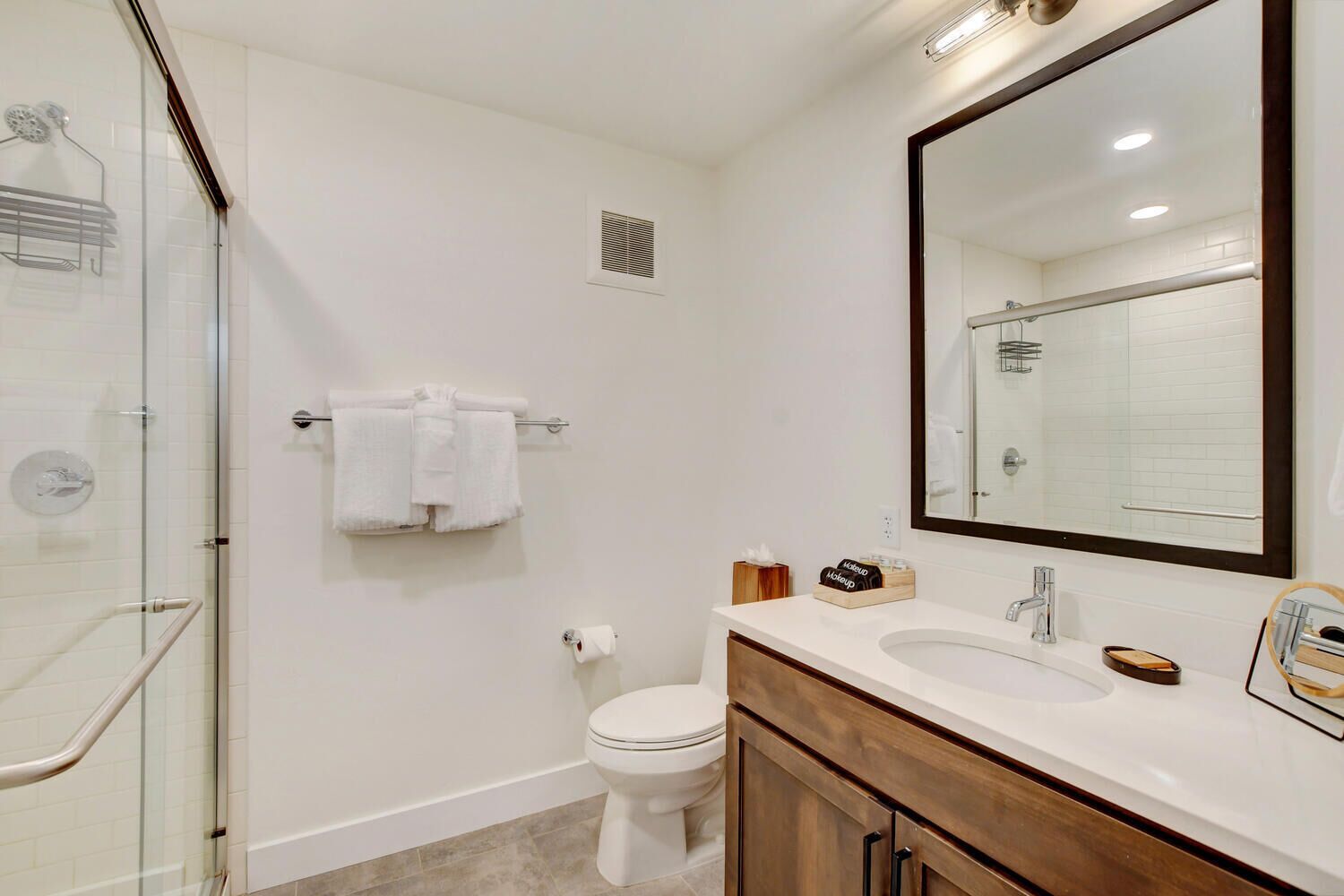 A modern bathroom with a glass shower enclosure, a white toilet, a vanity with a mirror, and a towel rack.