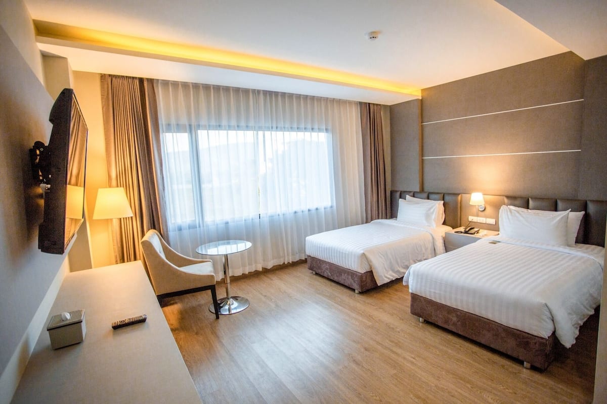 A hotel room with two beds, a desk, a chair, and a small table.
