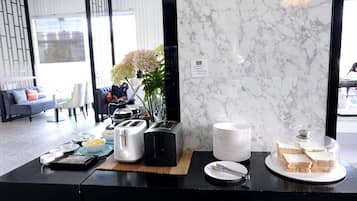 Un buffet per la colazione con macchina del caffè, tostapane, piatti, ciotole e pane.