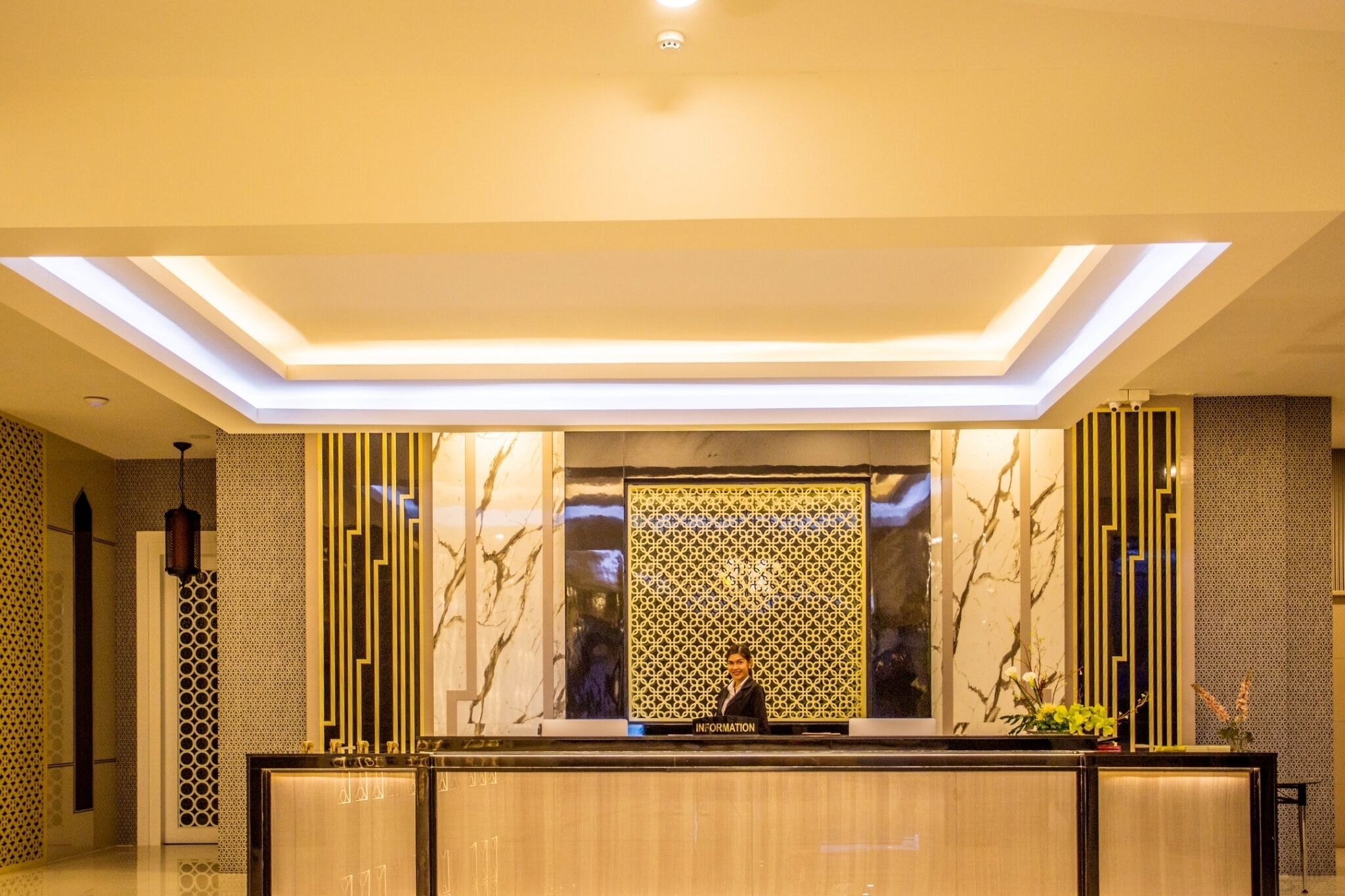 A hotel reception area with a modern design, featuring a reception desk, a patterned wall, and a ceiling with recessed lighting.
