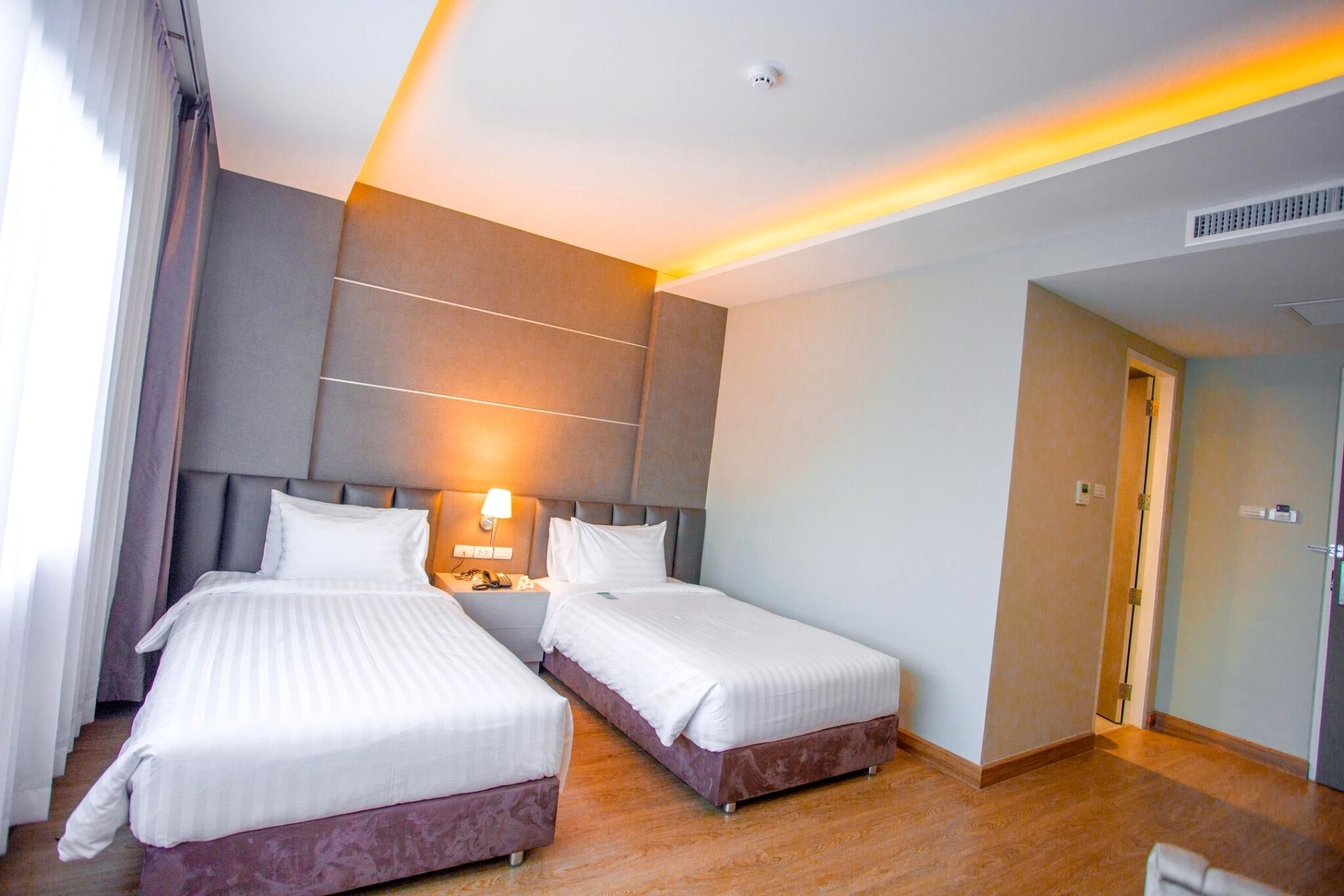 A hotel room with two beds, a nightstand, a lamp, and a door.