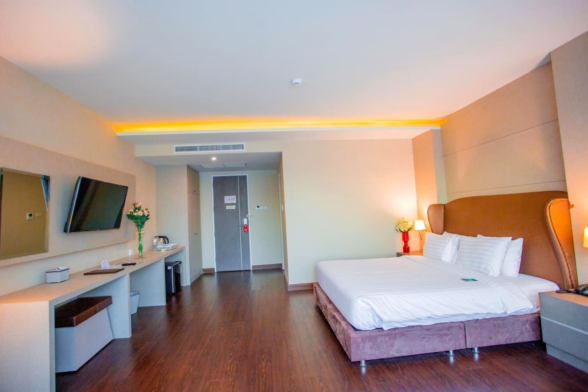A hotel room with a bed, bedside table, lamp, and a TV mounted on the wall.