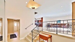 Un amplio salón con una escalera, un banco de madera y una alfombra estampada.