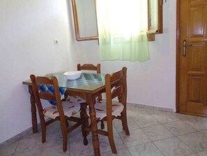 Un comedor con una mesa de vidrio, cuatro sillas de madera, un cuenco blanco y una cortina verde.