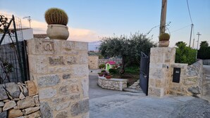 A stone gate leading to a courtyard with a cactus, potted plants, and a small house with a red roof. - Pet-Friendly Apartment 'I due ulivi' with view on the hills of Modica, Terrace & Wi-Fi (Modica)