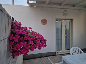 A patio area with a white table and chair, a door with a glass panel, and a wall-mounted plaque.