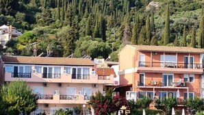 A coastal hotel with multiple-story buildings, a pool area, and a backdrop of a forested hillside.
