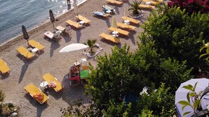 A beach with sun loungers and umbrellas, a pier with boats, and a building with a red roof.