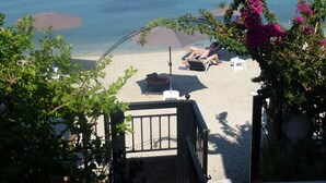 A beach with a person sunbathing, a chair, and a small boat.