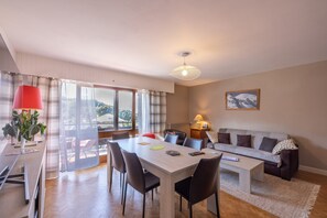 Un coin repas avec une table, des chaises et une lampe rouge. On aperçoit un canapé et une lampe posée sur une table d’appoint à l’arrière-plan.