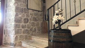 A stone wall with a framed picture, a wooden barrel with flowers, and a staircase with a metal railing. - Private Stone House Next to the sea (Kotor)