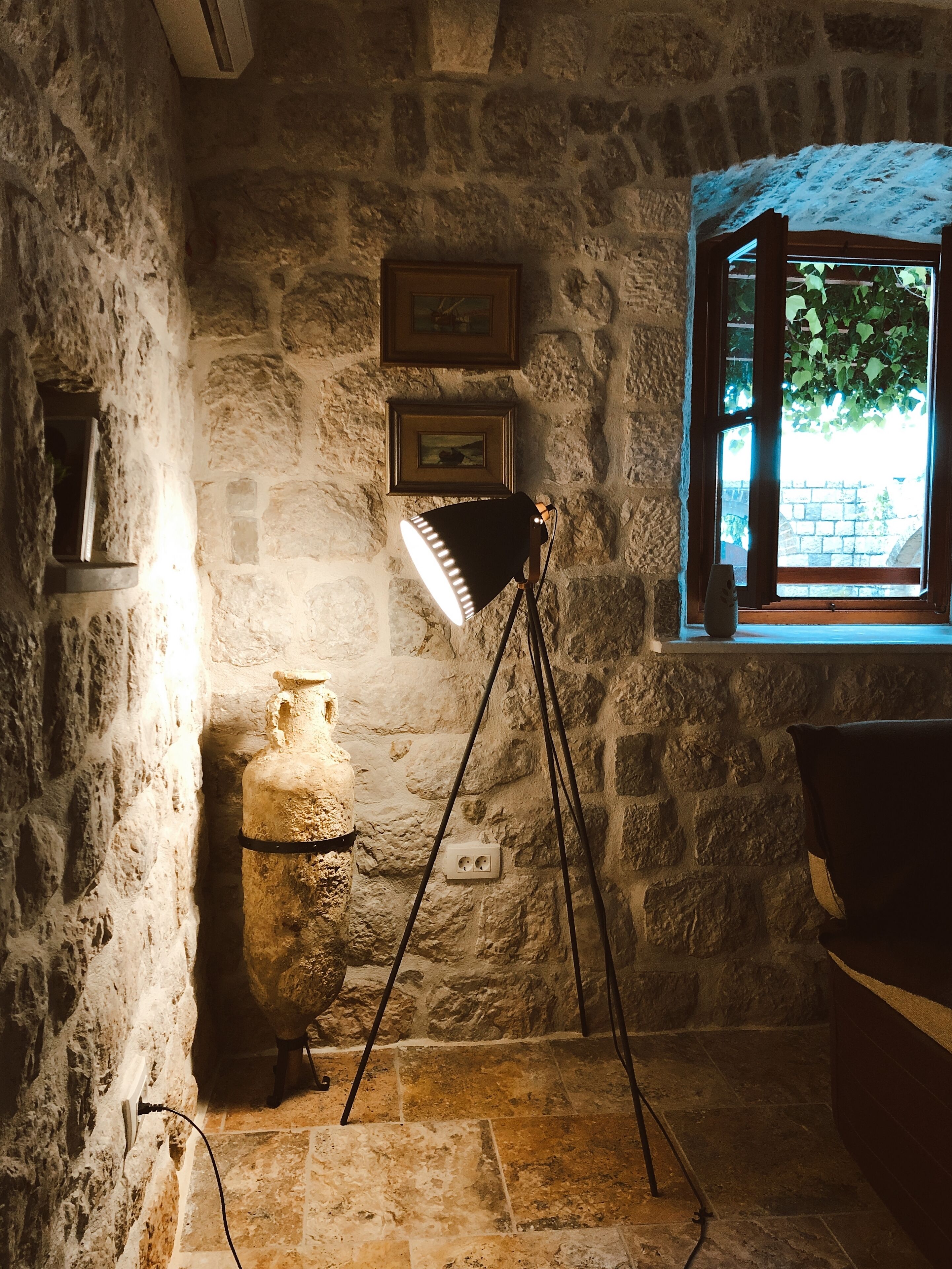 A stone-walled room with a single window, a lamp, and a stone sculpture.