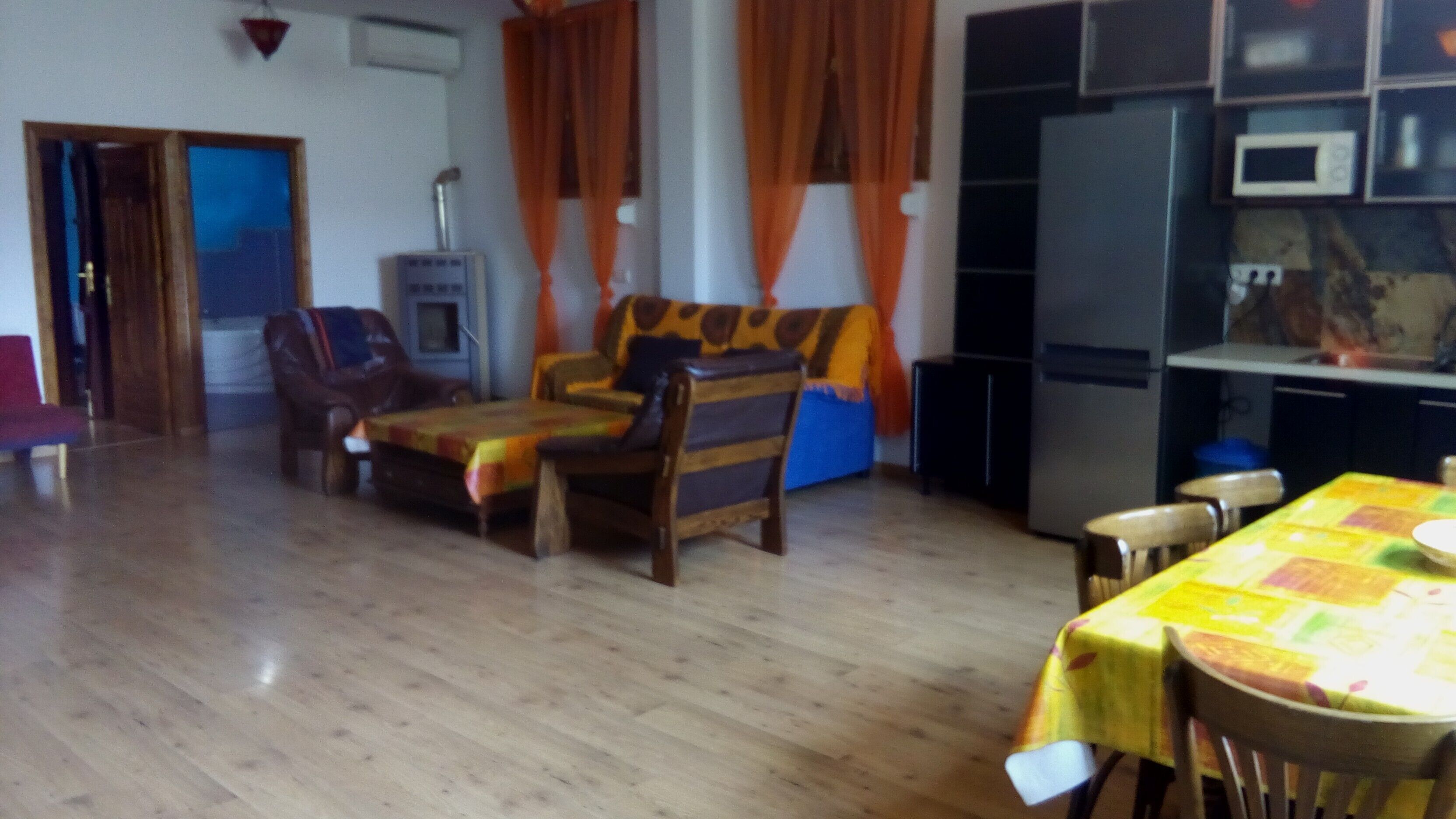 Ein Wohnzimmer mit einer Couch, Sesseln, einem Esstisch und einer Küchenzeile mit Geräten.