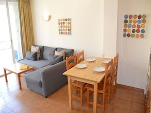 A living room with a sofa, a dining table set for four, and two wall art pieces.