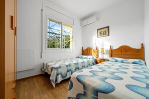 A bedroom with two beds, a window with a view, a wooden headboard, and a bedside table with a lamp. - 'Villa Amador' with Sea View, Pool & Wi-Fi (L'Ampolla)