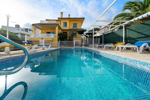 A swimming pool with tiled edges, a white fence, and a yellow building in the background. - 'Villa Amador' with Sea View, Pool & Wi-Fi (L'Ampolla)