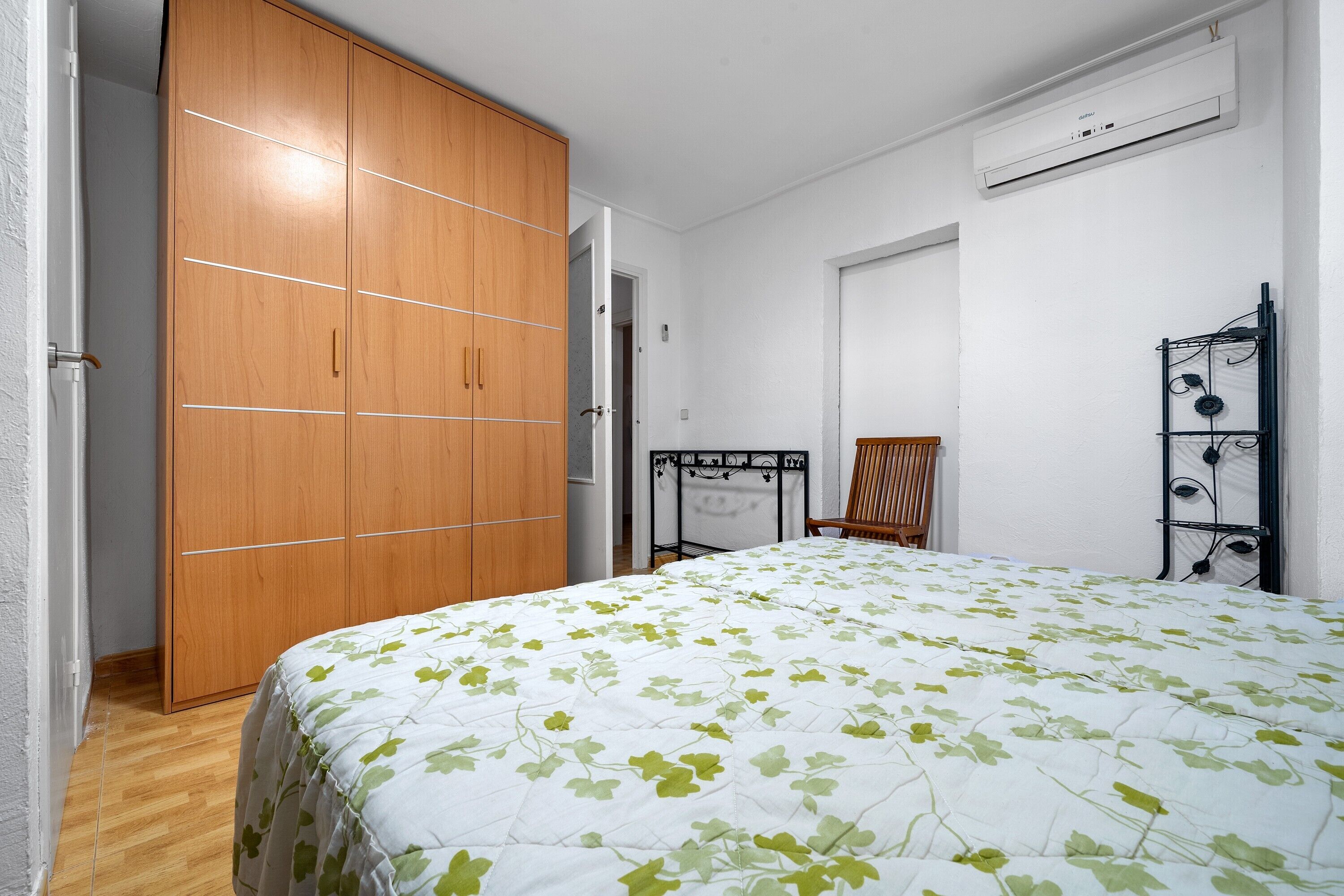 Ein Schlafzimmer mit Bett, Kleiderschrank, Sessel und einer an der Wand befestigten Ablage.