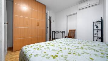 Ein Schlafzimmer mit Bett, Kleiderschrank, Sessel und einer an der Wand befestigten Ablage.