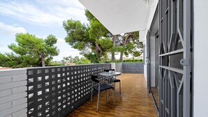 Een overdekt terras buiten met een tafel en stoelen, een houten vloer en een witte muur met een lattenwerkstructuur.