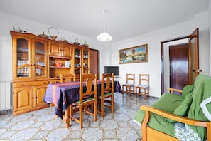 Un coin repas comprenant un buffet en bois, une table recouverte d’une nappe, des chaises et un téléviseur.