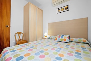 Une chambre à coucher avec un lit, une armoire en bois, une chaise et une table de chevet avec une lampe.