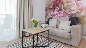 A living room with a sofa, a small table, a vase of flowers, and a large floral wall mural.