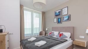A neatly made bed with a grey blanket, a bedside table with a lamp, and a wall with framed pictures.