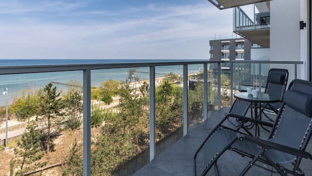 A balcony with a view of the sea, a table with chairs, and a glass railing.