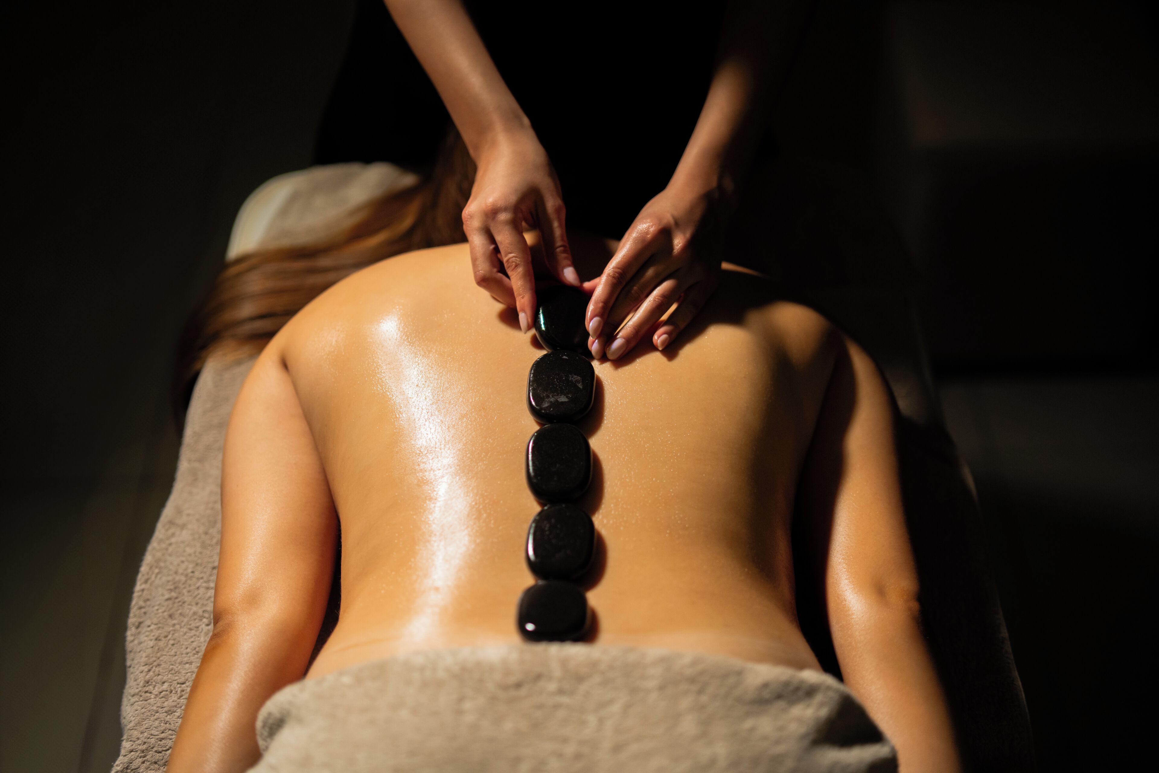 A person receiving a back treatment with black stones.