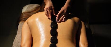 A person receiving a back treatment with black stones.