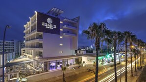 A modern hotel with a prominent sign, multiple floors, and a well-lit outdoor area with tables and chairs. - Gaia Sun N Blue Hotel (Ayia Napa)