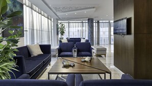 A modern hotel lobby with a seating area, large windows, and a flat-screen TV on the wall. - Gaia Sun N Blue Hotel (Ayia Napa)