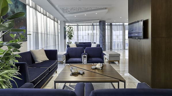 A modern hotel lobby with a seating area, large windows, and a flat-screen TV on the wall. - Gaia Sun N Blue Hotel (Ayia Napa)