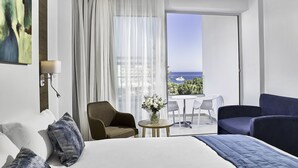 A hotel room with a bed, a sitting area with a table and chairs, a view of the sea, and a balcony with a table and chairs. - Gaia Sun N Blue Hotel (Ayia Napa)
