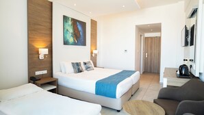 A hotel room with a large bed, a smaller bed, a sofa, a coffee table, and a painting on the wall. - Gaia Sun N Blue Hotel (Ayia Napa)