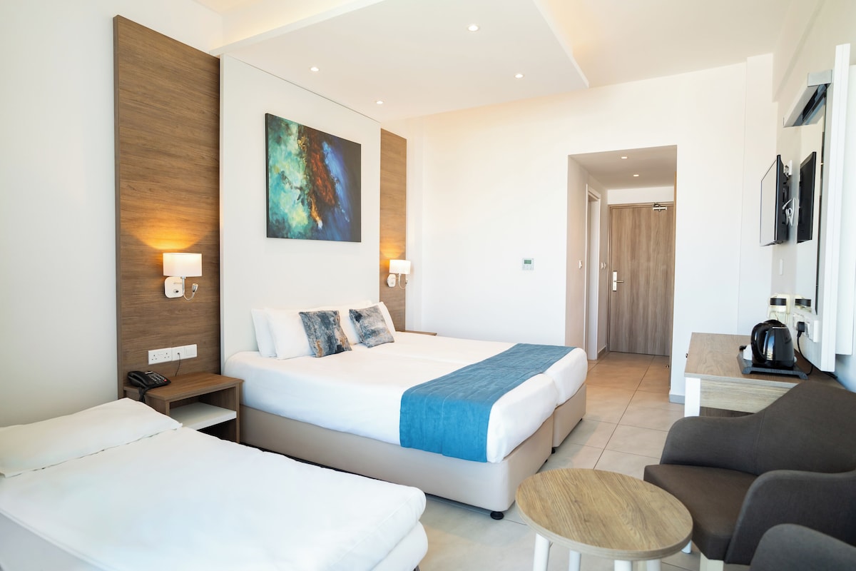 A hotel room with a large bed, a smaller bed, a sofa, a coffee table, and a painting on the wall.