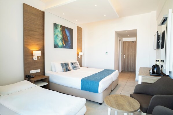 A hotel room with a large bed, a smaller bed, a sofa, a coffee table, and a painting on the wall. - Gaia Sun N Blue Hotel (Ayia Napa)