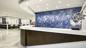Un área de recepción moderna con un mostrador curvo, un cuadro abstracto azul y una escultura metálica.