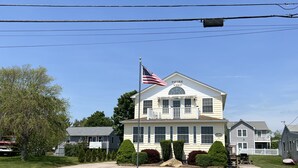 A two-story building with a white exterior, a porch, and an American flag. - Water View " THE PIPERS NEST " - minutes to the beach, located in Snug harbour ! (South Kingstown)