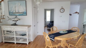 A dining area with a wooden table and chairs, a white cabinet with drawers, a ceiling fan, and a painting of a sailboat on the wall. - Water View " THE PIPERS NEST " - minutes to the beach, located in Snug harbour ! (South Kingstown)