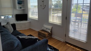 A living room with a blue sofa, a flat-screen TV, a decorative anchor, and a view through the windows. - Water View " THE PIPERS NEST " - minutes to the beach, located in Snug harbour ! (South Kingstown)