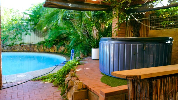 Ein Whirlpool, ein Schwimmbecken und eine Holzterrasse mit einer Pergola darüber.