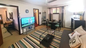 Ein Wohnzimmer mit Fernseher, Deckenventilator, Essbereich mit Stühlen und einer Couch.