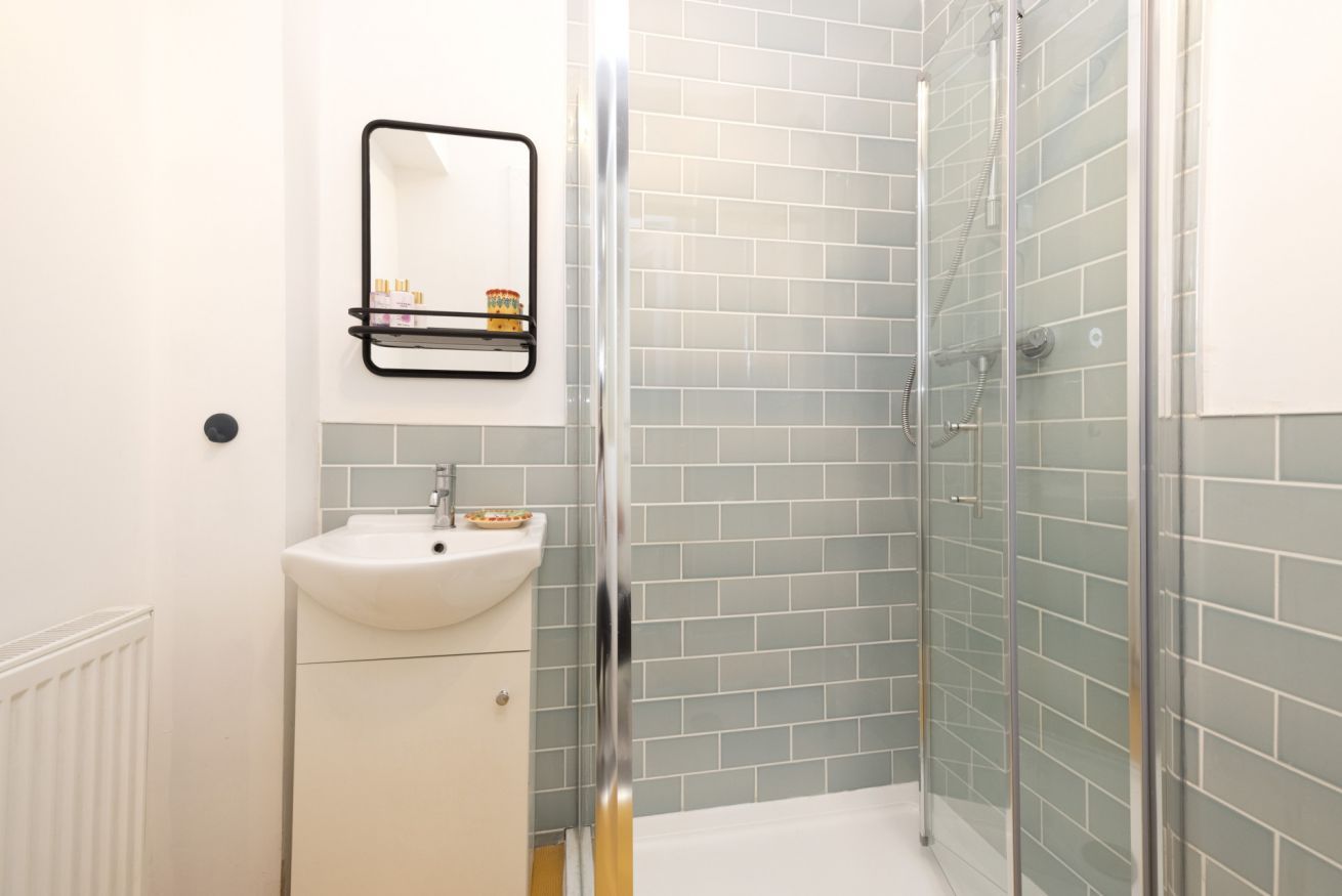 Ein modernes Badezimmer mit einer Duschkabine aus Glas, einem weißen Waschbecken und einem Spiegel darüber.