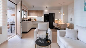 Eine moderne Küche mit weißen Schränken, ein Essbereich mit weißem Tisch und Stühlen sowie ein Wohnbereich mit weißem Sofa und Couchtisch.