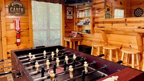 Un intérieur de chalet chaleureux avec une table de baby-foot, un téléviseur et un jeu de fléchettes.