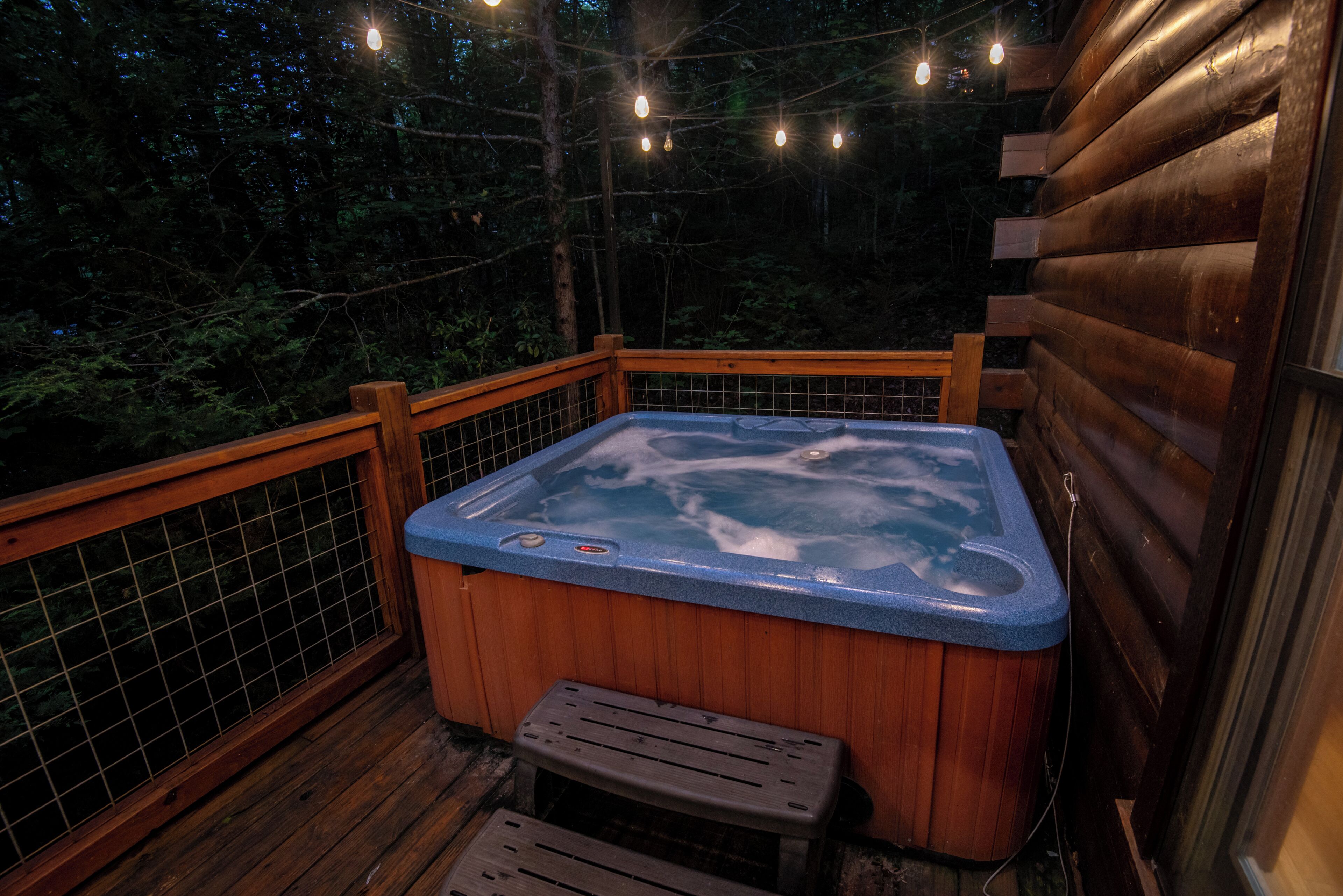 A wooden deck with a hot tub, surrounded by a wooden fence and string lights.